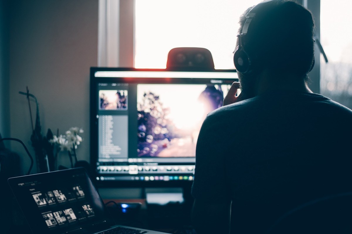 Un éditeur vidéo travaille sur un ordinateur, portant des écouteurs Un éditeur vidéo travaille sur un ordinateur, portant des écouteurs